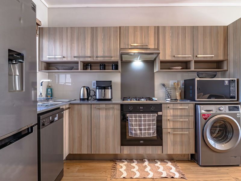 Modern kitchen featuring wood-grain cabinetry, integrated appliances, stainless steel oven and hob, and durable laminate flooring in a clean, functional layout.