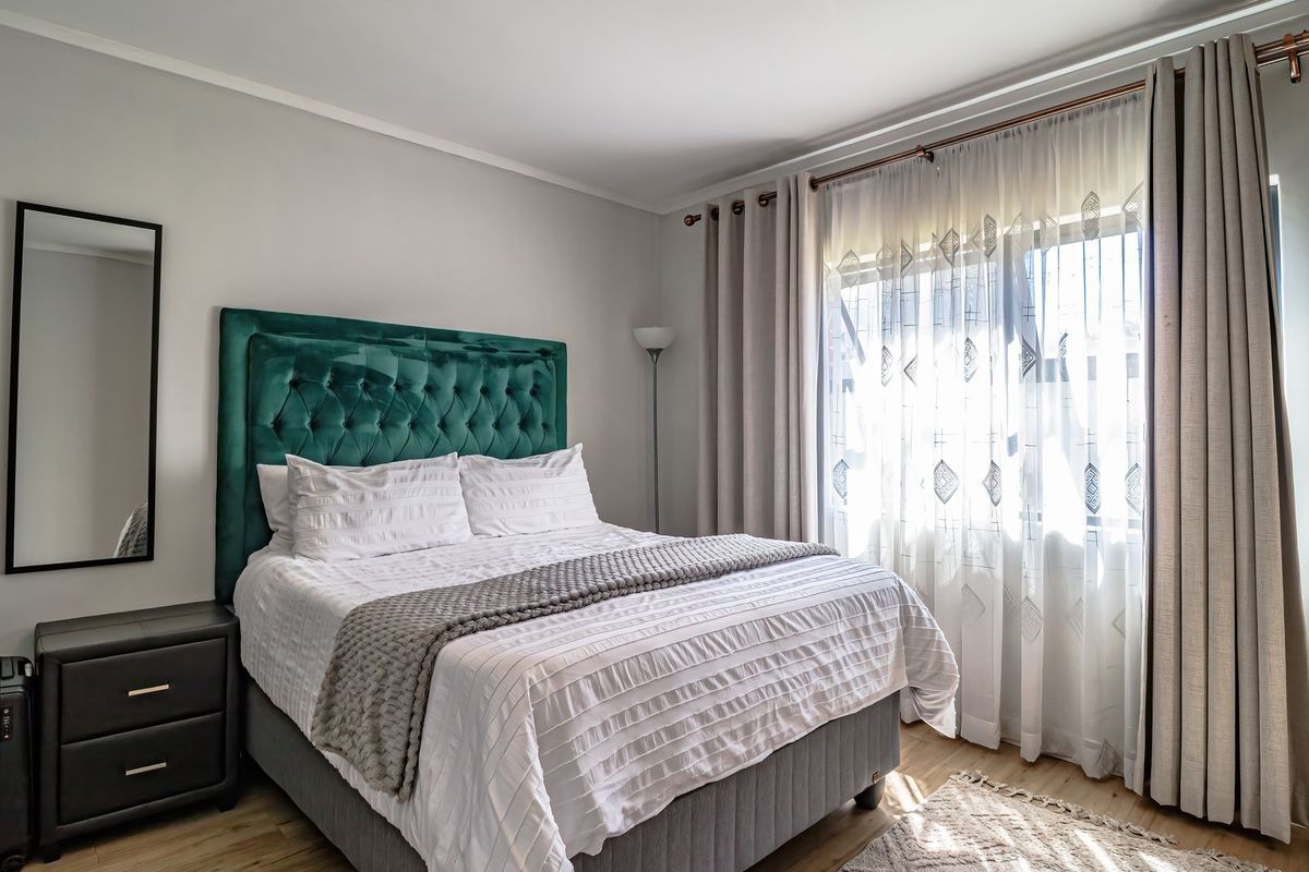 A well-maintained bedroom featuring laminate flooring, neutral wall finishes, and a large window with installed curtain rods.