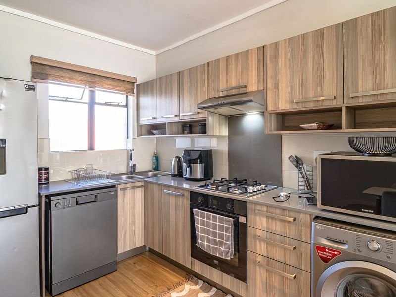 A well-maintained kitchen featuring modern wood-look cabinetry, integrated stainless steel appliances, a gas hob, and a tiled splashback with ample counter space.