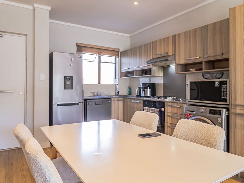 Modern open-plan kitchen featuring wood-finish cabinetry, integrated appliances, and durable laminate flooring, seamlessly flowing into the dining area.