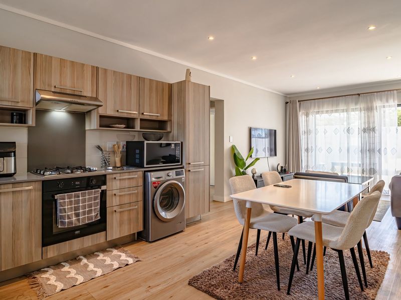 Modern open-plan living area featuring a well-appointed kitchen with wood-finish cabinetry, integrated appliances, and seamless flow to a bright, light-filled lounge space.