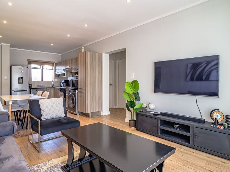 A modern open-plan living and kitchen area featuring laminate flooring, recessed lighting, and contemporary built-in cabinetry with integrated appliances.