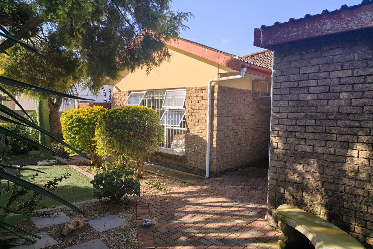 Rear exterior view of the property featuring brick wall construction, paved pathways, and established garden area with security fencing.