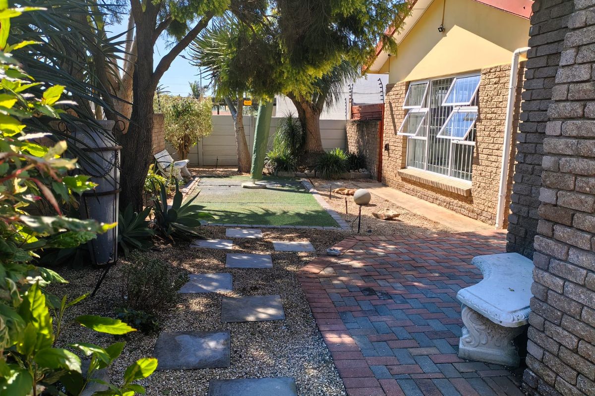 A well-maintained rear garden area featuring brick paving, artificial lawn, and established trees alongside the facebrick exterior of the house.