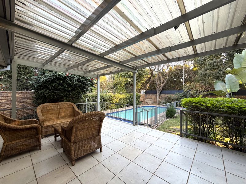 Covered outdoor patio featuring tiled flooring and a metal roof structure, overlooking a private swimming pool and garden area.