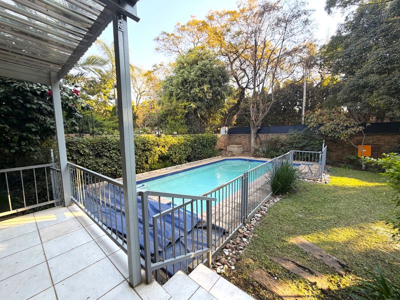 Outdoor pool area featuring a fenced swimming pool, tiled patio, and established garden with brick boundary walls.