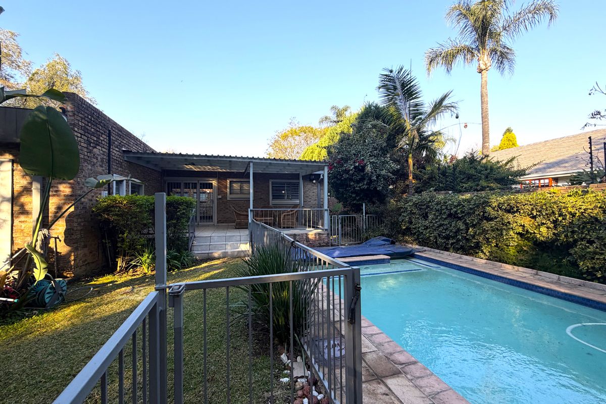 Rear exterior view featuring a swimming pool with safety fencing, a covered patio area, and established garden landscaping.