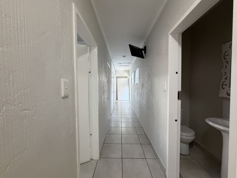 A long, tiled hallway providing access to multiple rooms, featuring neutral wall finishes and recessed lighting.