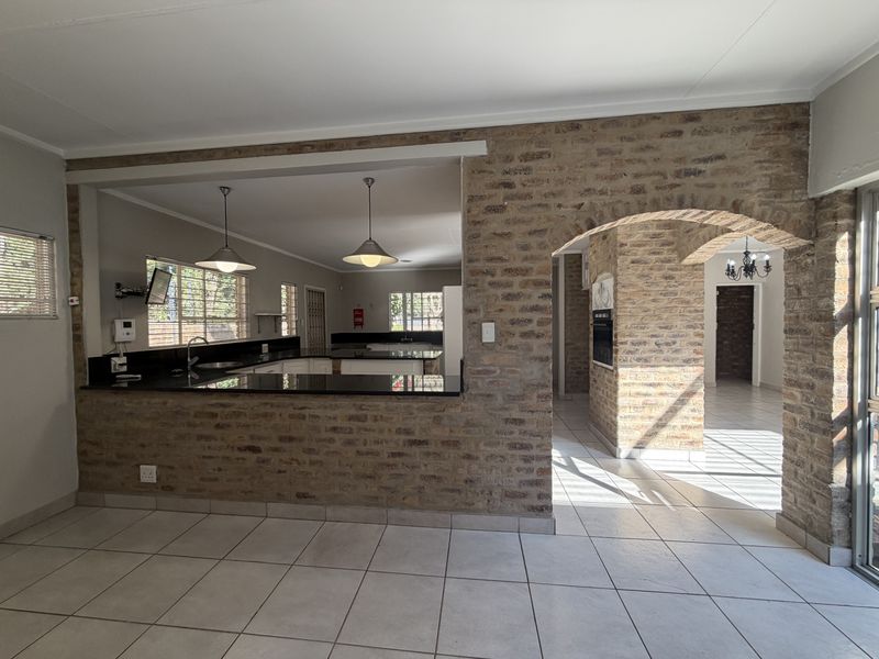 Spacious open-plan living and kitchen area featuring exposed brick walls, an elegant brick archway, granite countertops, and neutral ceramic floor tiles.