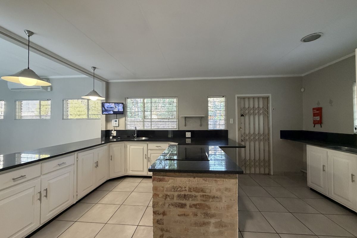 Spacious kitchen featuring white cabinetry, dark granite countertops, a central island with an exposed brick base, and tiled flooring.
