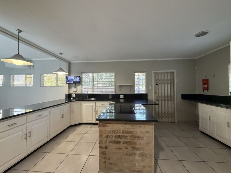 Spacious kitchen featuring white cabinetry, dark granite countertops, a central island with an exposed brick base, and tiled flooring.