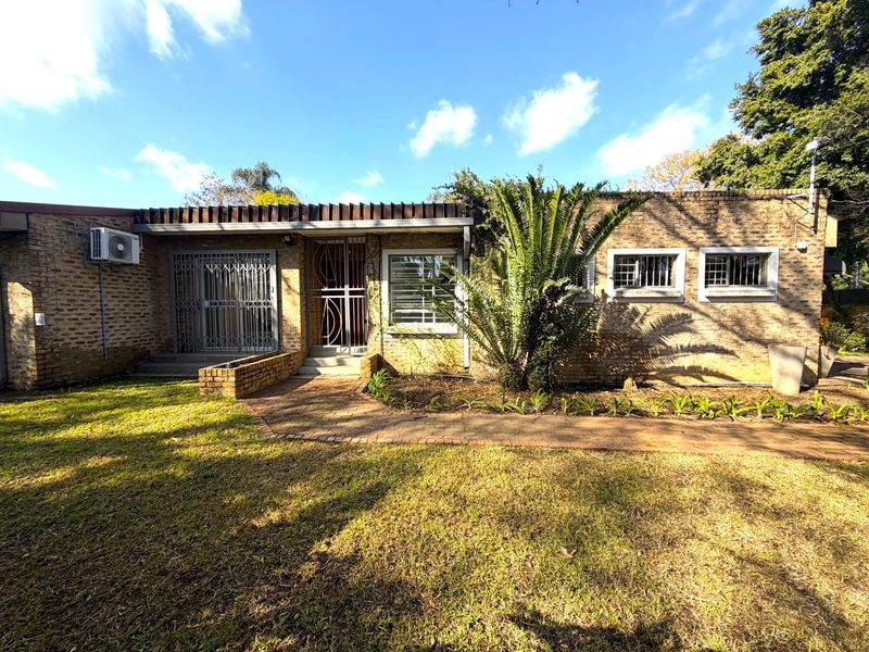 Rear view of a single-story brick house featuring a paved walkway, security gates, and an established garden area.