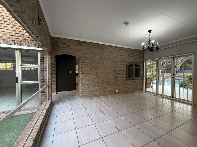 Spacious living area featuring exposed brick walls, tiled flooring, and large sliding glass doors providing access to the outdoor pool area.