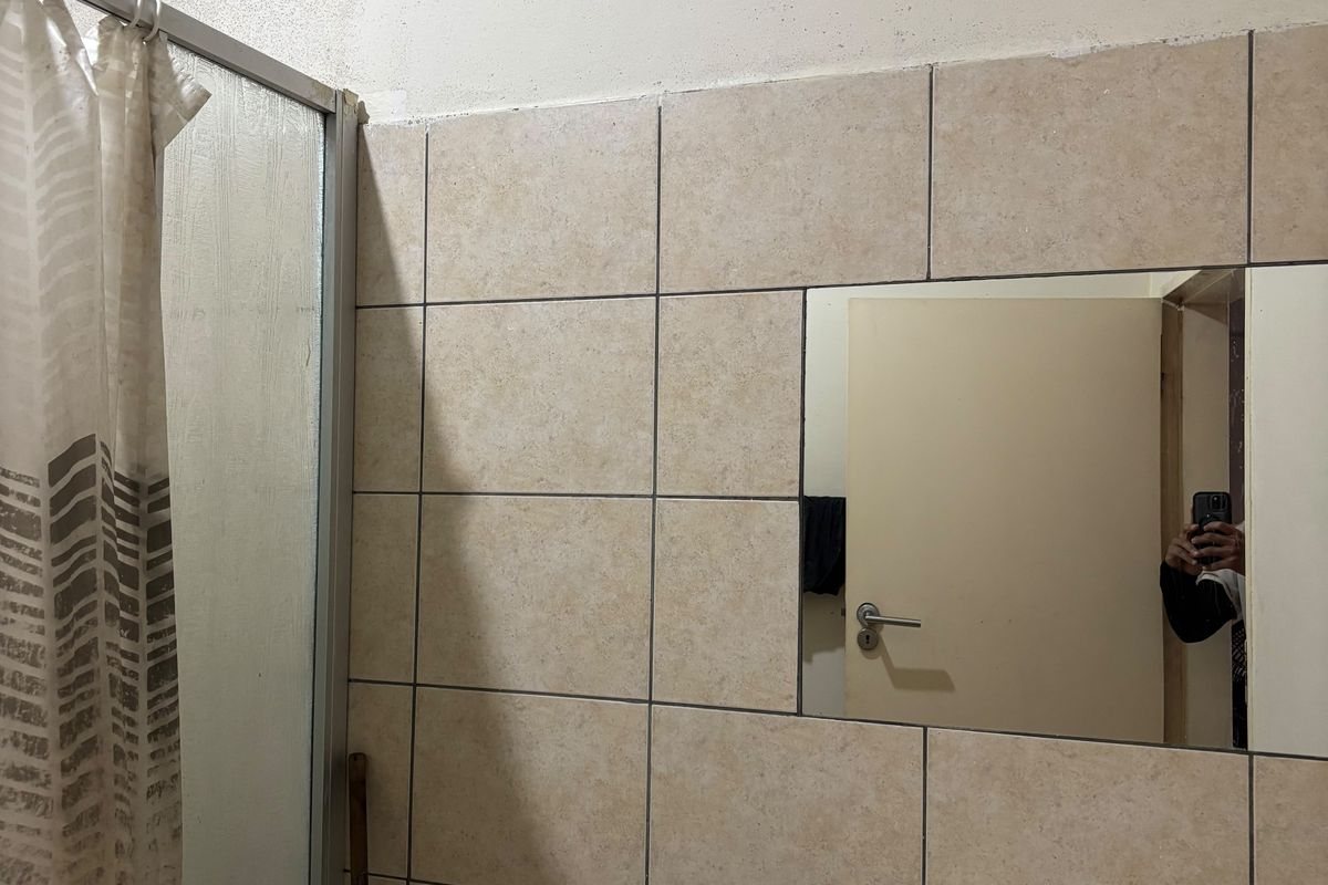 Bathroom featuring a shower enclosure, vanity basin with faucet, and wall-mounted mirror, showing signs of wear and ceiling staining.