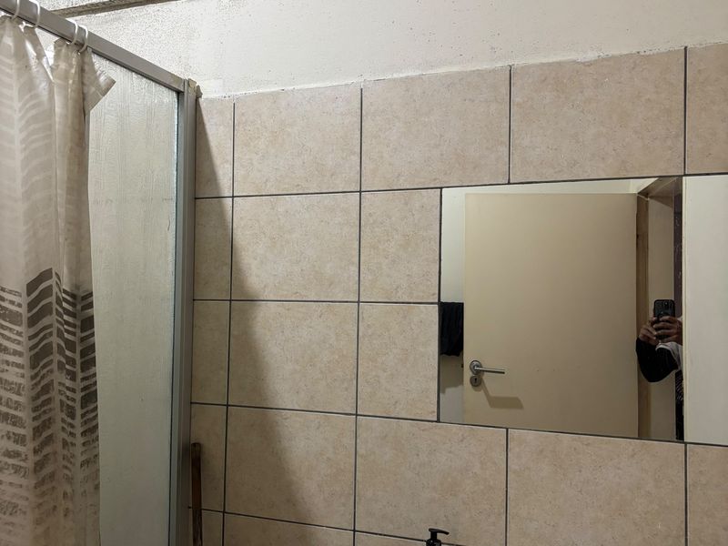 Bathroom featuring a shower enclosure, vanity basin with faucet, and wall-mounted mirror, showing signs of wear and ceiling staining.