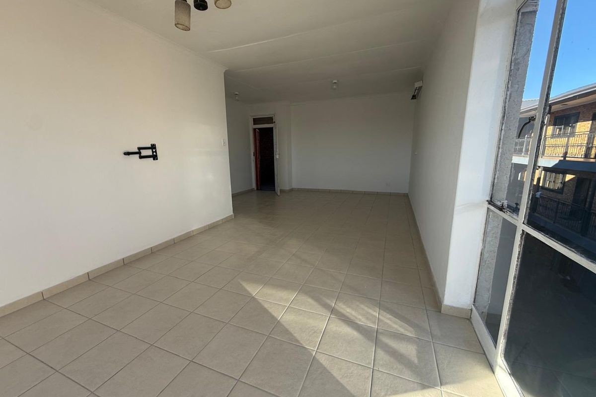 A spacious, empty living area featuring neutral tiled flooring, a wall-mounted television bracket, and a large glass sliding door providing natural light.