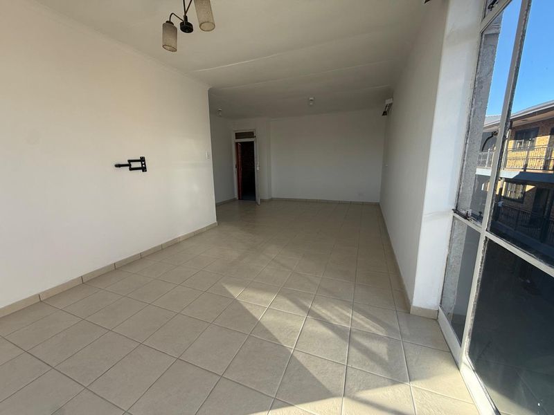 A spacious, empty living area featuring neutral tiled flooring, a wall-mounted television bracket, and a large glass sliding door providing natural light.