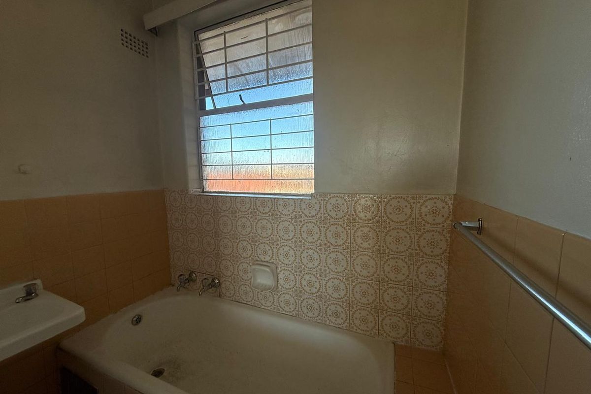 A dated bathroom featuring a standard bathtub, wall-mounted basin, and original patterned wall tiles, requiring modernization to improve aesthetic appeal.