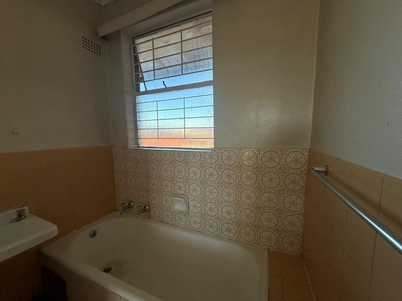 A dated bathroom featuring a standard bathtub, wall-mounted basin, and original patterned wall tiles, requiring modernization to improve aesthetic appeal.