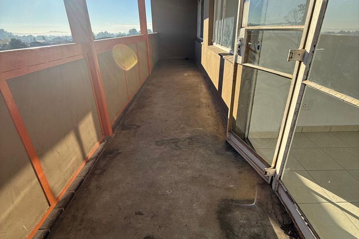 A long, open-air balcony with concrete flooring, metal railings, and direct access to the interior through a large sliding glass door.