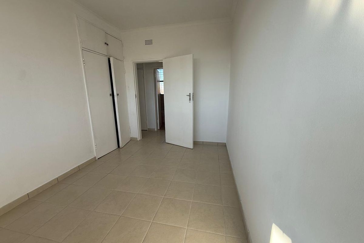 A clean, empty bedroom featuring neutral tiled flooring and built-in storage cupboards, offering a blank canvas for personalization.