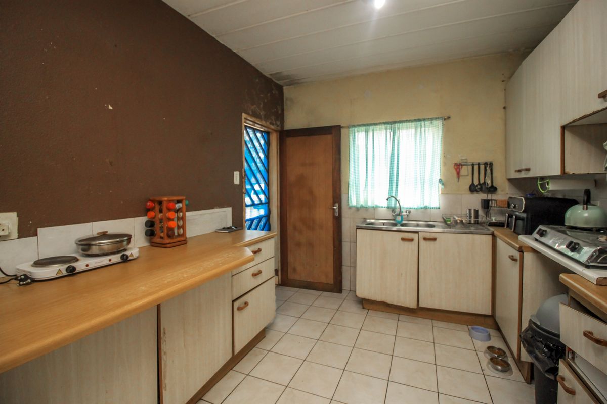 A dated kitchen featuring laminate countertops, built-in cabinetry, and tiled flooring, requiring cosmetic updates and surface repairs to modernize the space.