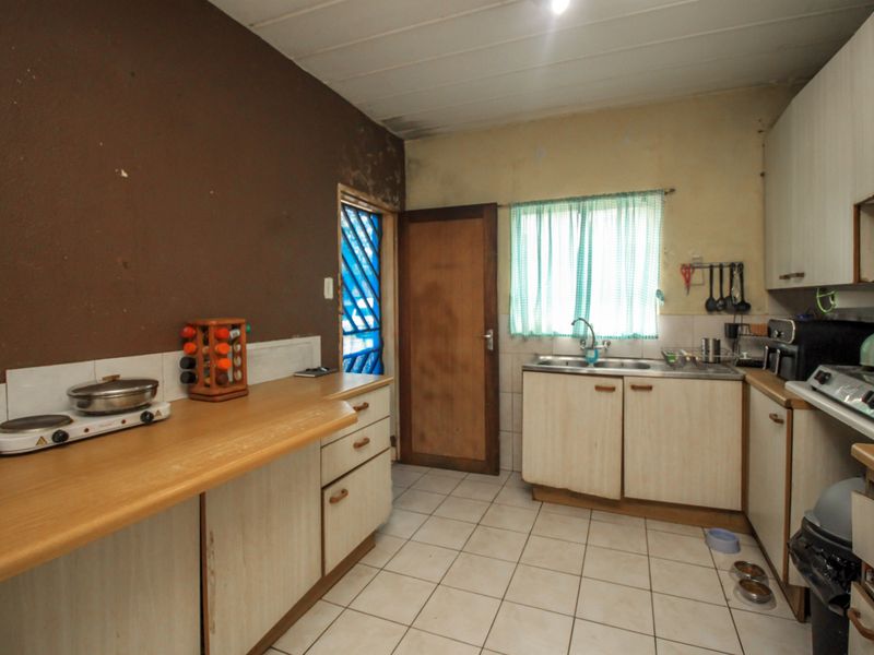 A dated kitchen featuring laminate countertops, built-in cabinetry, and tiled flooring, requiring cosmetic updates and surface repairs to modernize the space.