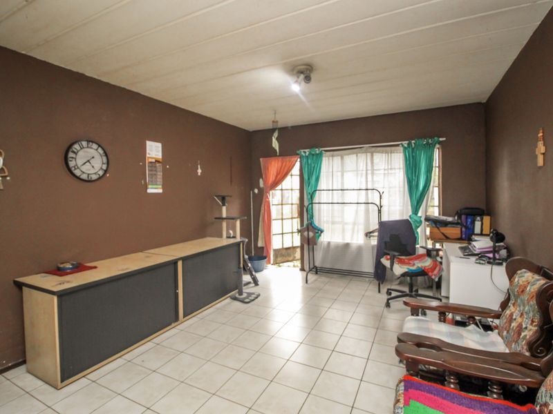 A living room featuring tiled flooring, dark brown walls, and a sliding glass door providing access to the exterior.