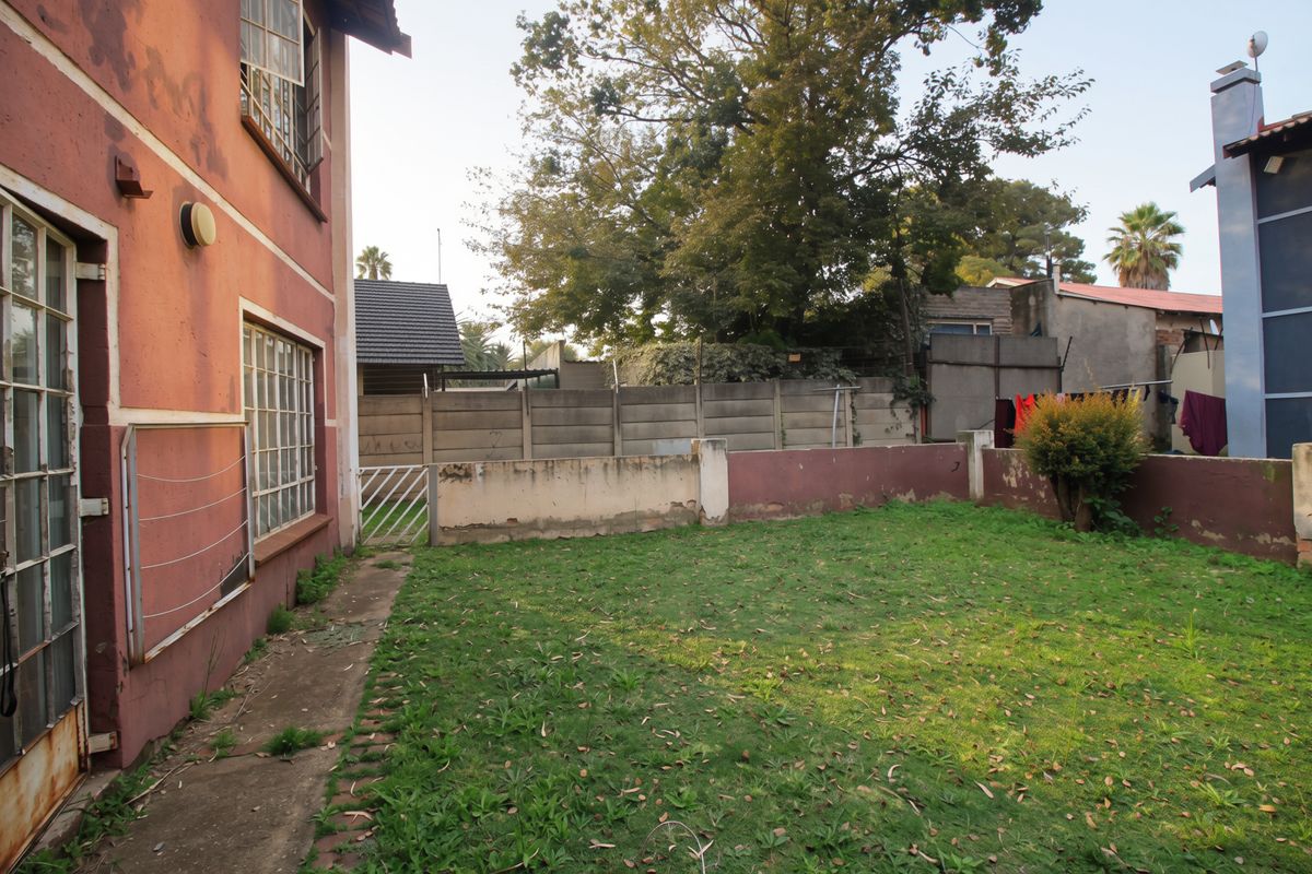 Rear exterior view of the apartment featuring a private garden area, precast concrete boundary walls, and a paved pathway along the building facade.