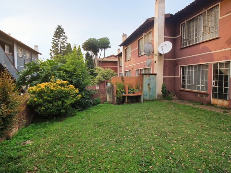 Rear view of the apartment building featuring a private lawn area, brick facade, and steel-framed windows showing signs of weathering.