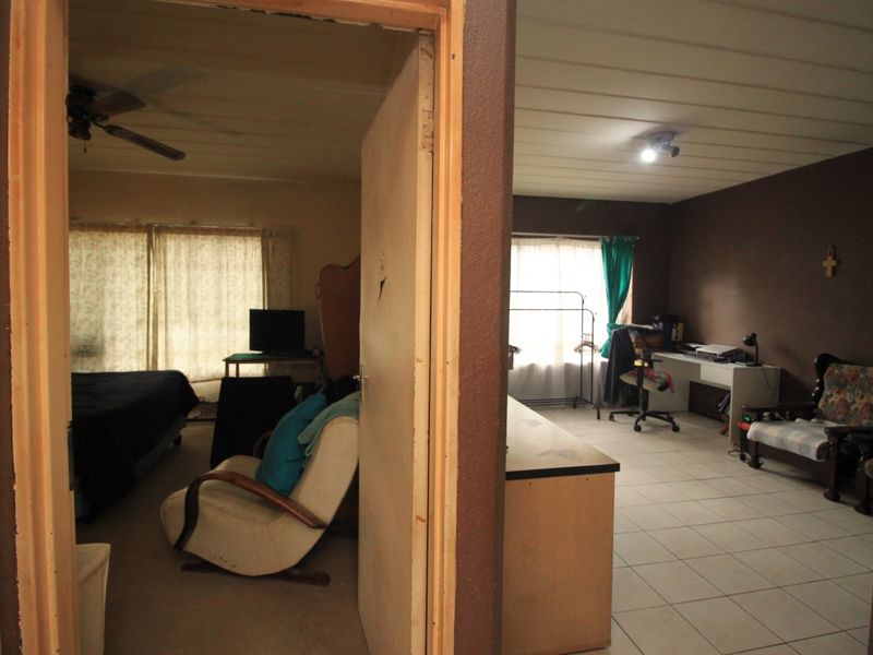 A view through a doorway showing two connected rooms with tiled and carpeted flooring, featuring a ceiling fan and dated interior finishes.