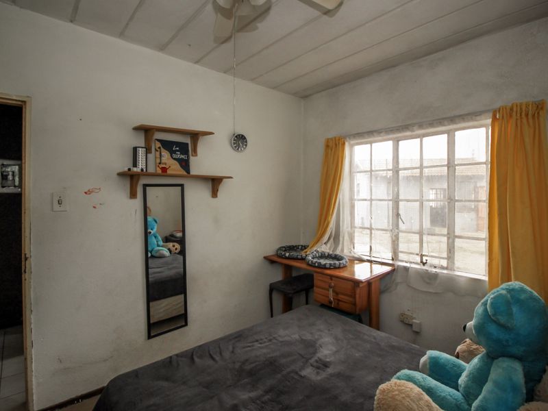 A bedroom featuring a steel-framed window, ceiling fan, and built-in shelving, requiring cosmetic updates to the walls and ceiling finishes.
