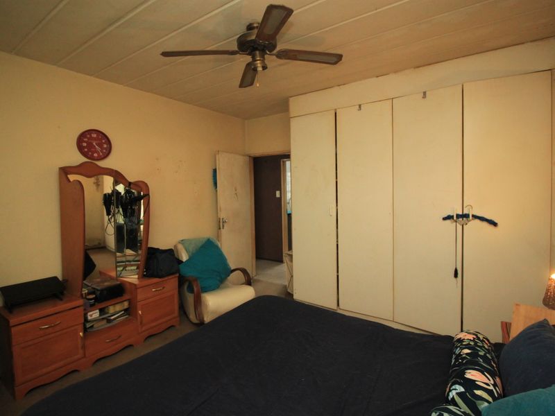 A bedroom featuring a large built-in wardrobe and a ceiling fan, requiring cosmetic updates to improve the overall condition and aesthetic appeal.