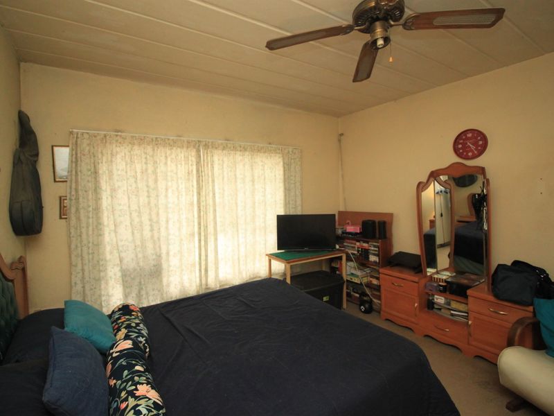 A bedroom featuring a ceiling fan and large window with curtains, requiring cosmetic updates to modernize the space.