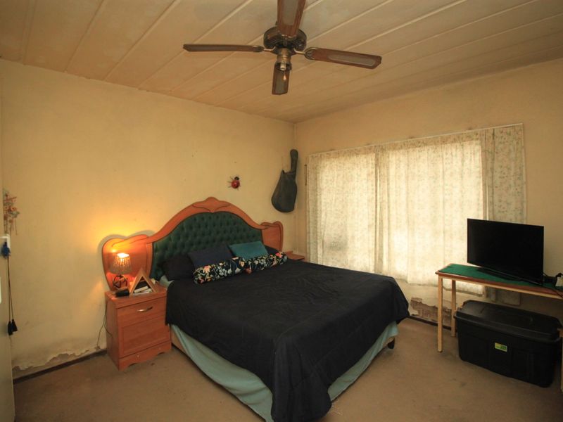 A bedroom featuring a ceiling fan, showing significant signs of wear including damaged wall plaster and peeling paint, requiring cosmetic renovation.