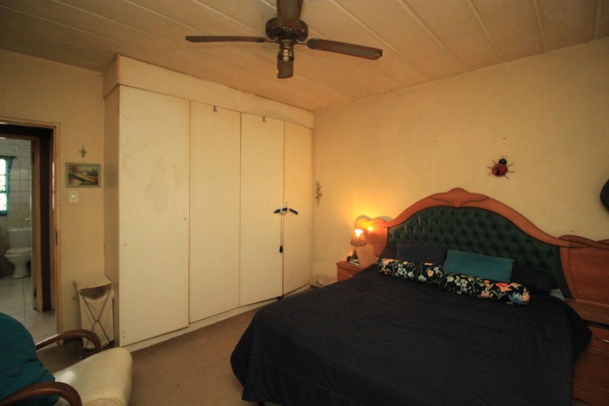 A bedroom featuring built-in cupboards, a ceiling fan, and timber panel ceiling. The space requires cosmetic updates to improve its overall condition.
