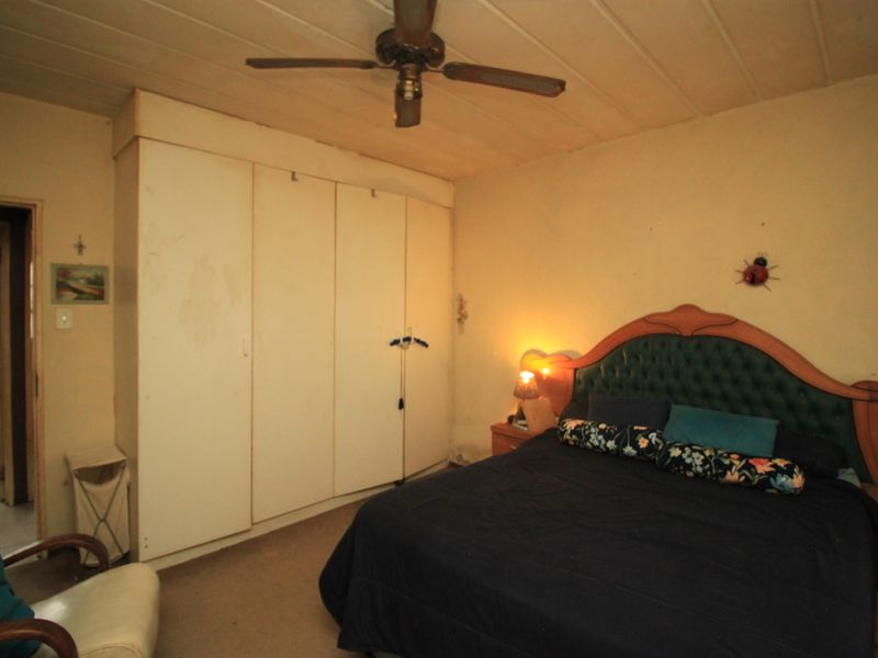 A bedroom featuring built-in cupboards, a ceiling fan, and timber panel ceiling. The space requires cosmetic updates to improve its overall condition.