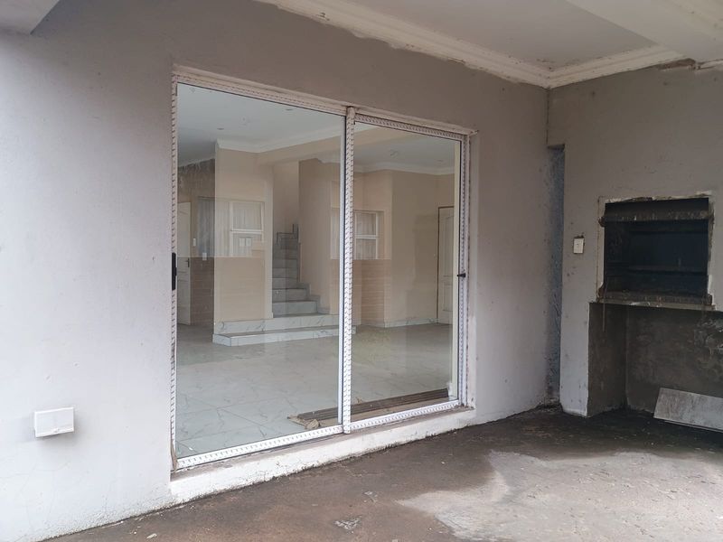 Covered patio area featuring a built-in braai, sliding glass doors leading to the interior, and tiled flooring, currently in need of finishing touches.