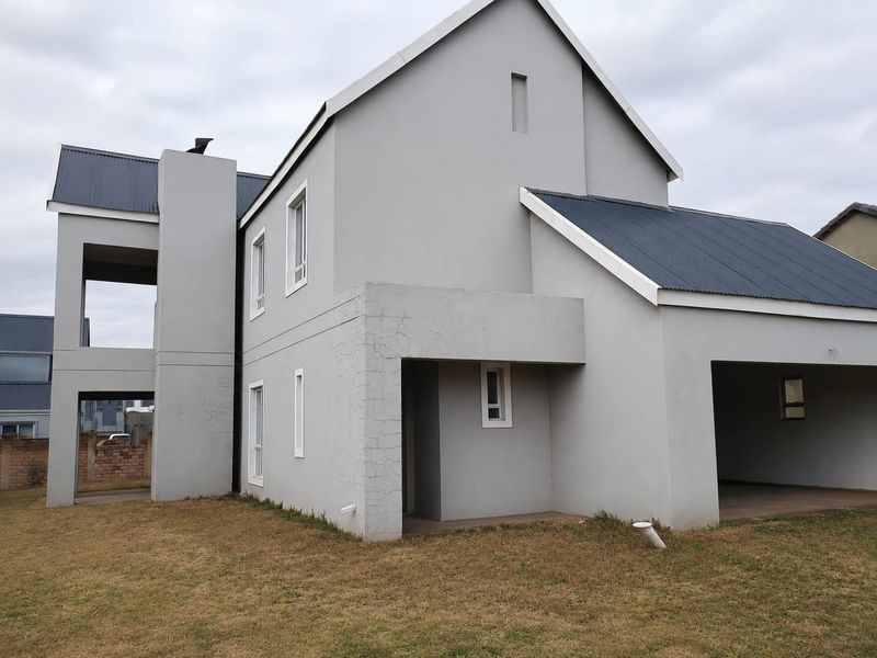 Rear view of a modern townhouse featuring a grey plastered facade, corrugated metal roofing, a covered patio area, and an integrated garage.