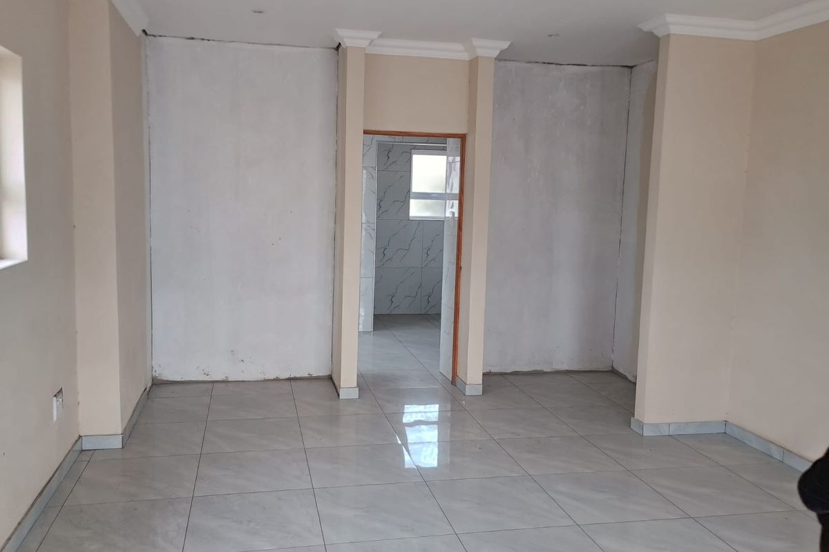 An empty living area featuring neutral porcelain floor tiles, recessed lighting, and decorative cornicing, currently requiring final wall finishing and painting.