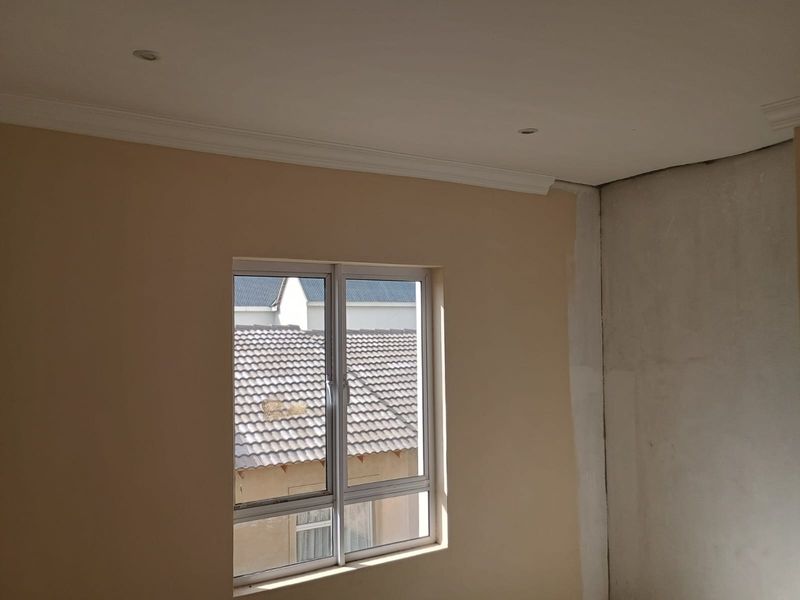 An empty bedroom featuring an aluminium window, recessed downlights, and ceiling cornices, currently requiring wall finishing and painting to complete the space.