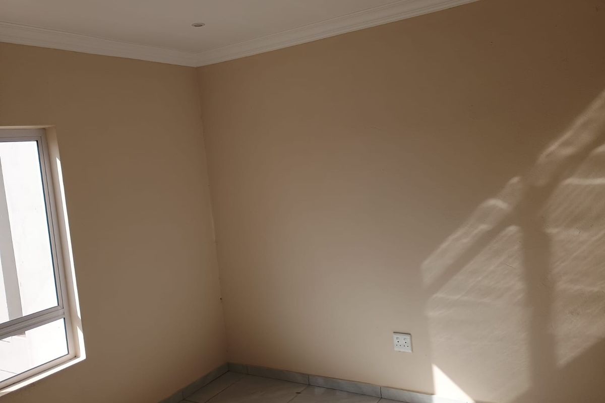 A bright, empty bedroom featuring tiled flooring, neutral wall finishes, and an aluminium-framed window, providing a clean canvas for interior design.