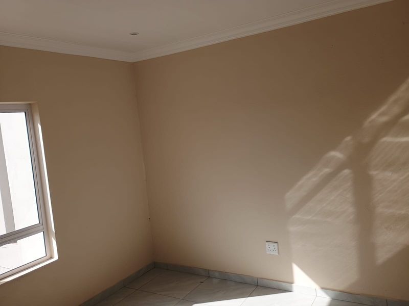 A bright, empty bedroom featuring tiled flooring, neutral wall finishes, and an aluminium-framed window, providing a clean canvas for interior design.