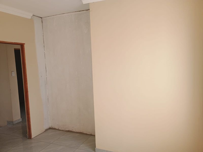 An empty hallway area featuring tiled flooring and a wooden door frame, currently showing unfinished wall surfaces requiring cosmetic attention.