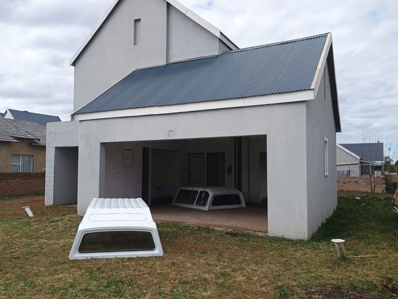Rear view of a double-story townhouse featuring a corrugated metal roof, plastered exterior walls, and an open-plan ground floor area.