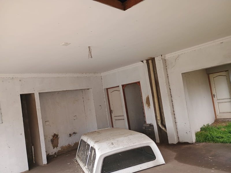 An unfinished or neglected garage space featuring exposed wiring, damaged wall plaster, and internal access doors.