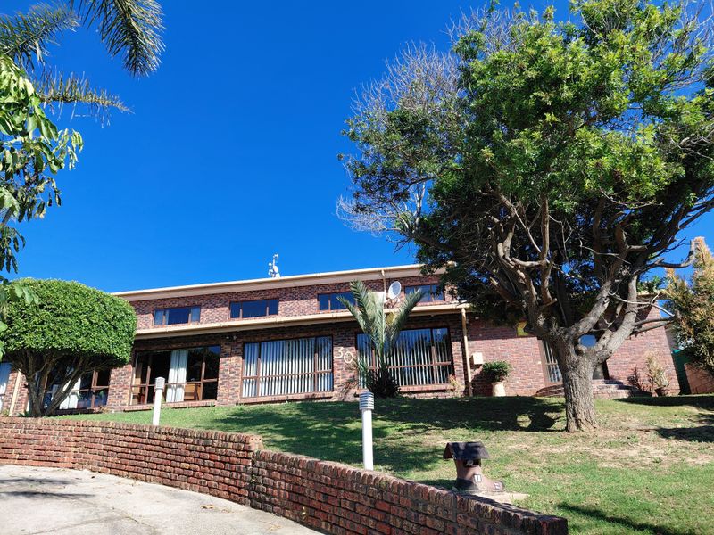 Front elevation of a brick-faced house featuring a terraced lawn, retaining wall, and large windows under a clear blue sky.