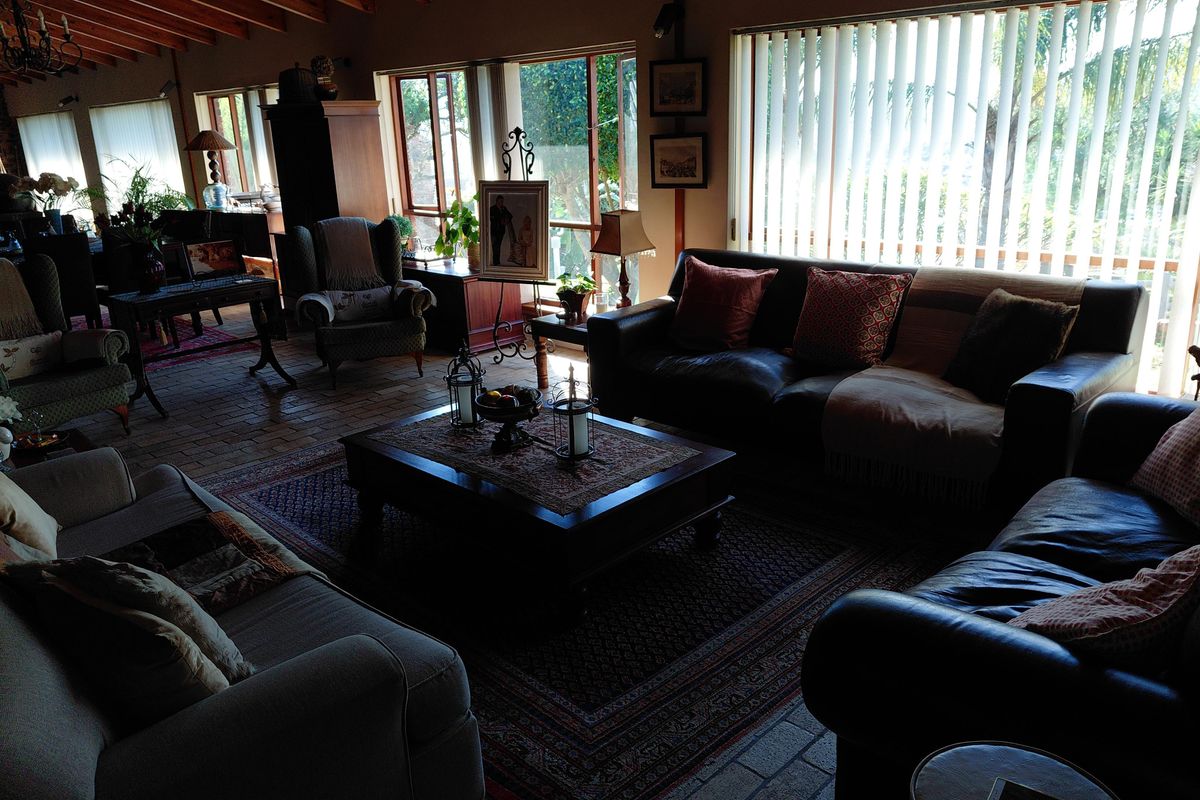 Spacious living room featuring exposed timber beam ceilings, traditional brick flooring, and large windows with vertical blinds allowing for natural light.