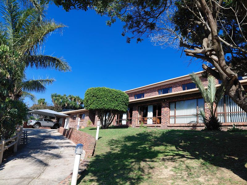 Front view of a brick house featuring a concrete driveway, carport, and established garden with large windows along the facade.