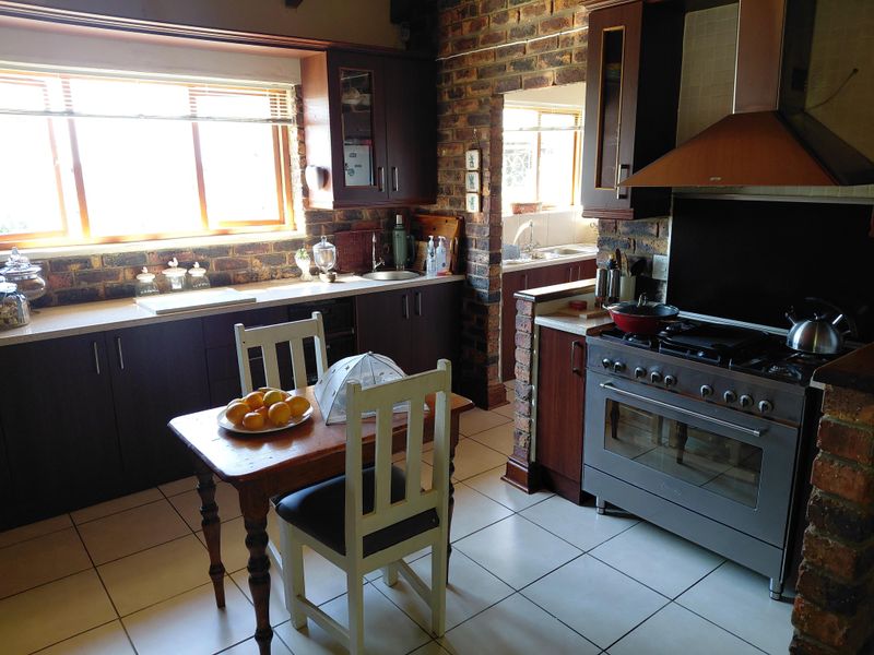 A rustic kitchen featuring exposed brick walls, dark cabinetry, a gas stove with extractor fan, and an adjoining scullery area with tiled flooring.